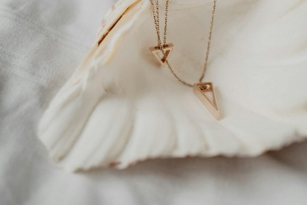 Two fine gold pendant necklaces resting on a white shell